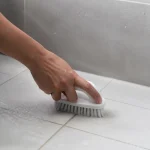 Main tenant brosse blanche nettoyant carrelage salle bain