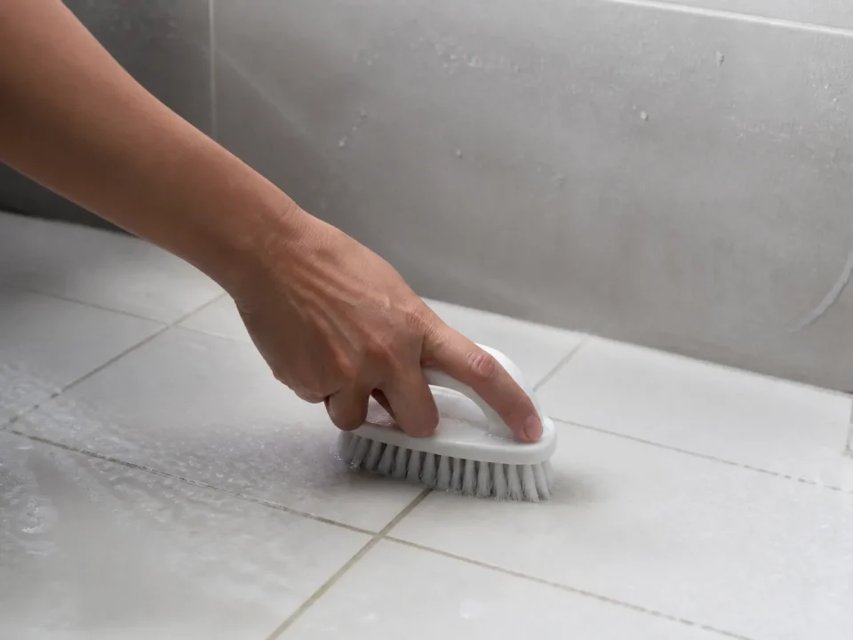Main tenant brosse blanche nettoyant carrelage salle bain