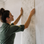 Personne collant feuille de papier peint sur mur blanc verticalement