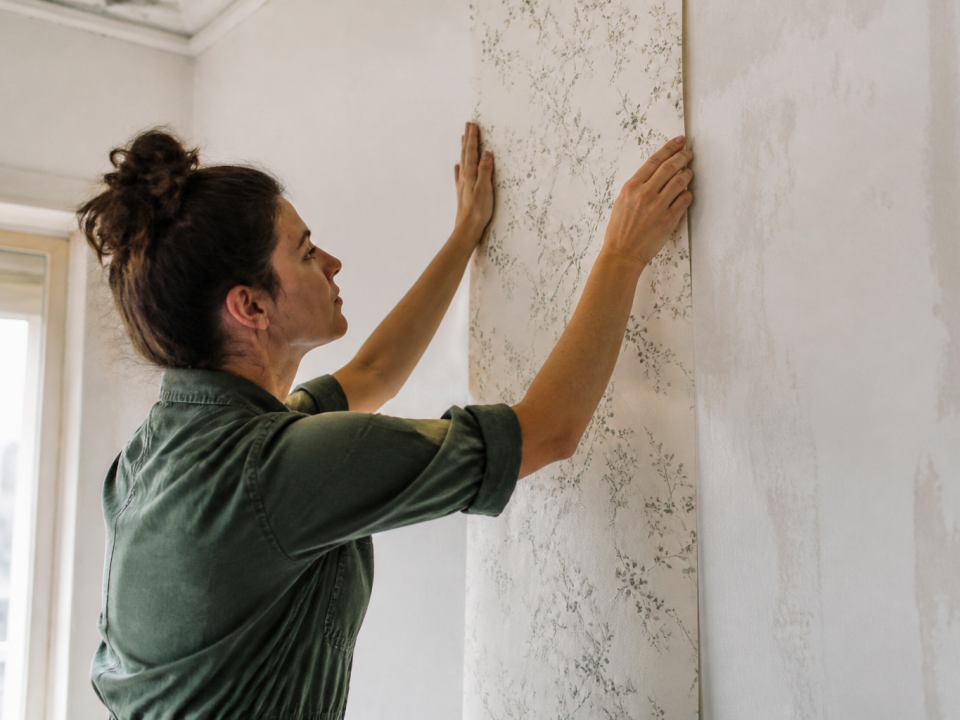 Personne collant feuille de papier peint sur mur blanc verticalement