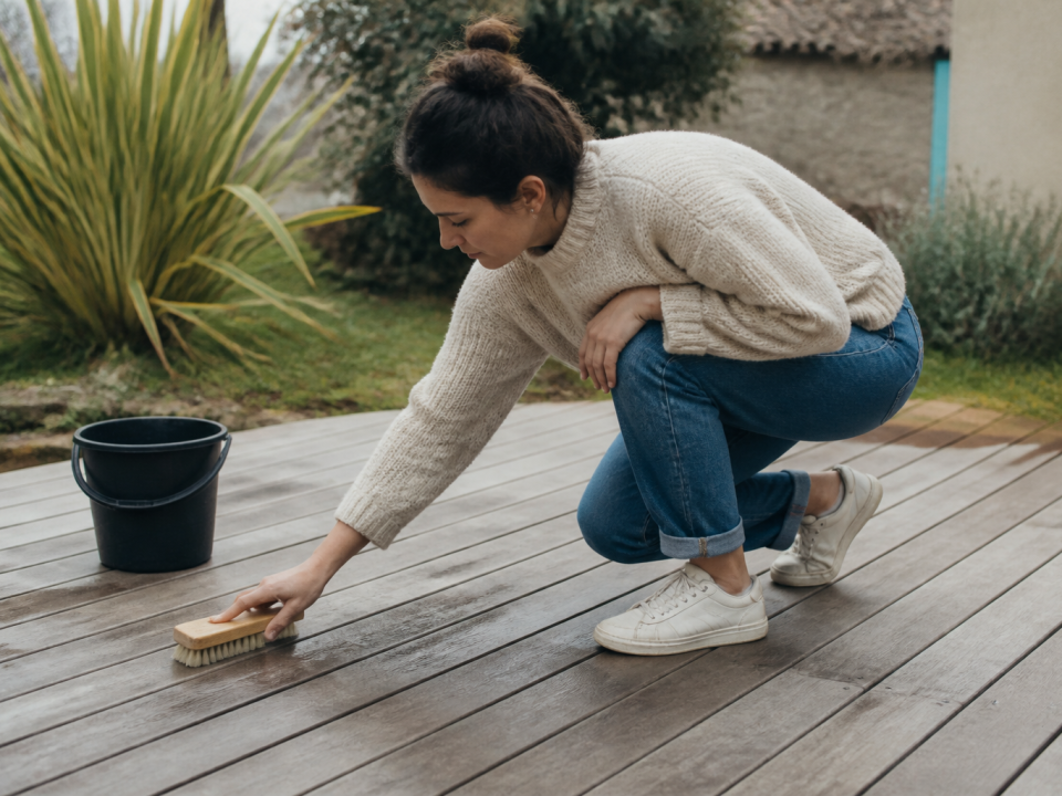 Personne accroupie recourant terrasse bois avec brosse