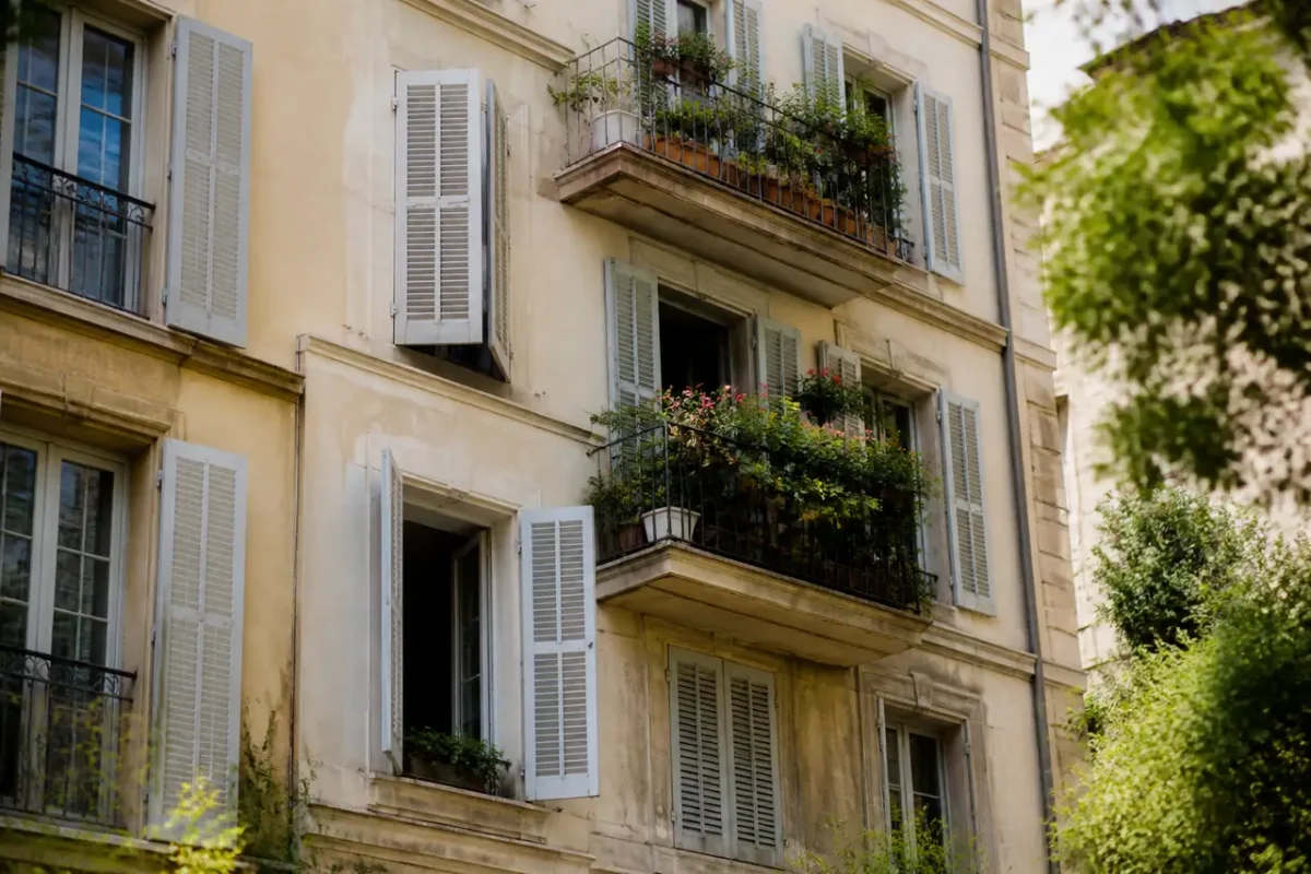 Immeuble ensoleille aux balcons fleuris et volets ouverts